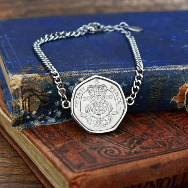 2000 twenty pence in a silver-coloured bracelet, crowned Tudor rose and date facing up, on old books