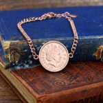 2002 one penny coin in a rose gold coloured bezel on a curb chain bracelet, resting on old blue and brown books