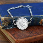 2003 coin showing the Queen Elizabeth II portrait in a round silver-tone bezel on a curb chain bracelet, on worn old books
