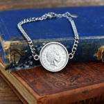 2006 coin showing the Queen Elizabeth II portrait in a round silver-tone bezel on a curb chain bracelet, on worn old books