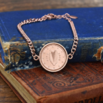 2006 Irish euro cent, harp ringed by twelve stars, in a rose gold-tone bracelet on old blue and tan books