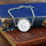 2009 coin showing the Queen Elizabeth II portrait in a round silver-tone bezel on a curb chain bracelet, on worn old books