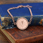 2009 Irish euro cent, harp ringed by twelve stars, in a rose gold-tone bracelet on old blue and tan books