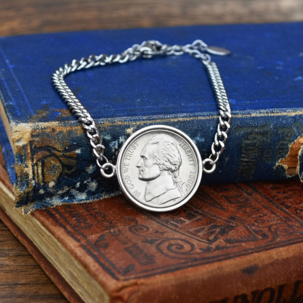 2009 US nickel set in a silver-coloured bezel on a silver curb chain bracelet, on two worn hardback books