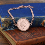 2010 one penny coin in a rose gold coloured bezel on a curb chain bracelet, resting on old blue and brown books