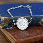 Silver-tone coin bracelet holding a 2011 Elizabeth II obverse, laid across worn blue and red hardback books