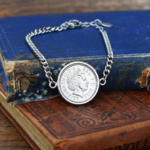 2012 coin with the Queen Elizabeth II portrait in a silver-tone bezel on a curb chain bracelet, on two old books