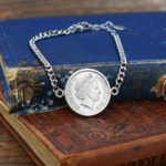 Australian coin dated 2013 showing the Elizabeth II portrait, in a silver-tone bracelet setting on worn blue and red books