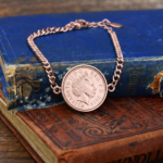 2013 one penny coin in a rose gold coloured bezel on a curb chain bracelet, resting on old blue and brown books