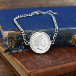 Australian coin dated 2014 with Elizabeth II portrait, set into a silver-tone curb chain bracelet on old blue and red books
