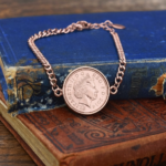 2014 one penny coin in a rose gold coloured bezel on a curb chain bracelet, resting on old blue and brown books