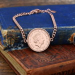 2015 one penny coin in a rose gold coloured bezel on a curb chain bracelet, resting on old blue and brown books