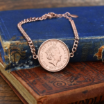 2017 penny showing the Queen Elizabeth II portrait in a rose gold-coloured bezel on a chain bracelet, on old books