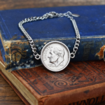 2018 US dime showing Roosevelt facing left in a silver-coloured bezel, curb chain bracelet on old books