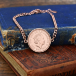 2019 penny showing the Queen Elizabeth II portrait in a rose gold-coloured bezel on a chain bracelet, on old books