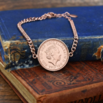 2020 penny showing the Queen Elizabeth II portrait in a rose gold-coloured bezel on a chain bracelet, on old books