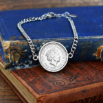 2022 coin with the crowned Queen Elizabeth II portrait in a silver-tone bezel on a curb chain bracelet, on old books