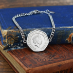 2022 twenty pence bracelet, seven-sided coin in a silver-coloured setting on a curb chain, on old books