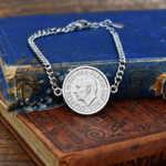 2023 coin with the King Charles III portrait facing left, silver-tone bezel and curb chain bracelet, on old books