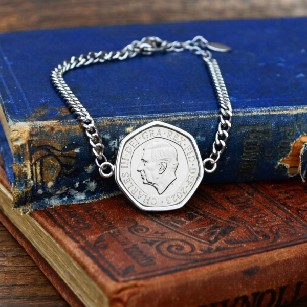 2023 twenty pence bracelet in a silver-coloured setting, curb chain and lobster clasp, on faded blue and red books