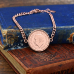 2024 penny showing the King Charles III portrait in a rose gold-coloured bezel on a chain bracelet, on old books