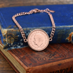 2025 penny showing the King Charles III portrait in a rose gold-coloured bezel on a chain bracelet, on old books