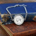 2025 US nickel in a silver-coloured bezel on a curb chain bracelet, resting on old blue and tan books
