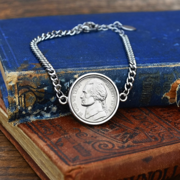 2025 US nickel in a silver-coloured bezel on a curb chain bracelet, resting on old blue and tan books