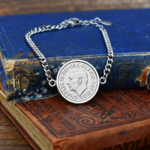 Silver-tone coin bracelet holding a 2026 King Charles III obverse in a plain bezel, on worn blue and red books