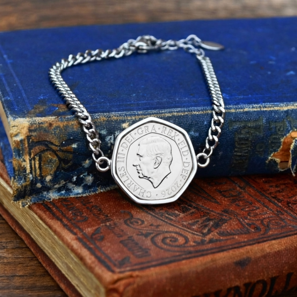 2026 twenty pence bracelet, seven-sided coin in a silver-coloured setting on a curb chain, on old books