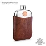 Copper Australian coin on a pewter hip flask held in a brown leather sleeve, white background