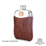 Pewter hip flask in a brown leather sleeve at an angle, copper Australian coin set above the leather